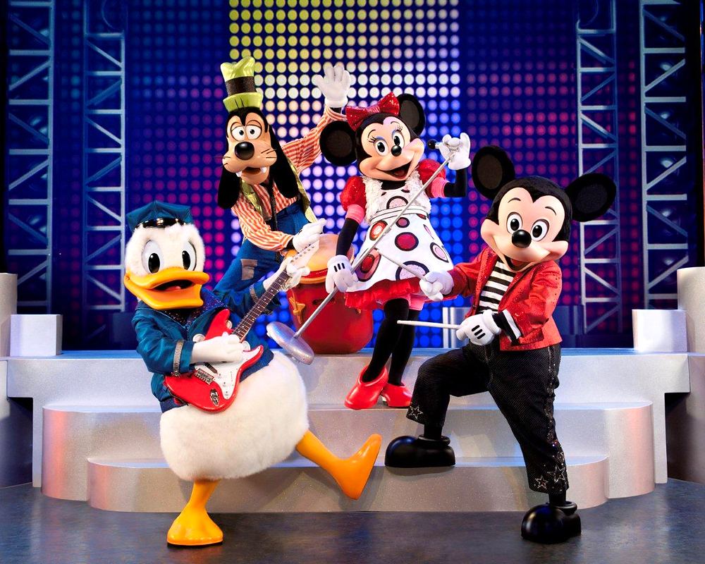 Donald, Goofy, Minnie and Mickey in rock outfits with guitars on a lit stage, Mickey's Music Festival. Costume design by Cynthia Nordstrom