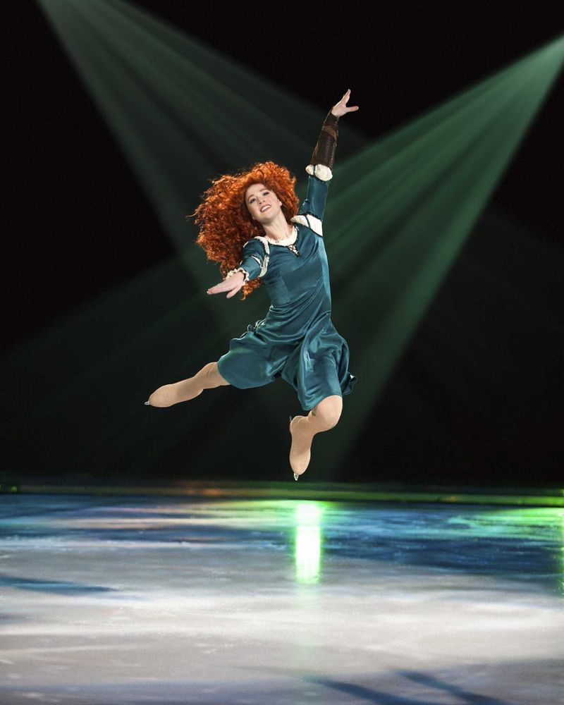 Merida with wild red curls in a teal gown leaping on ice under green light, Rockin' Ever After. Costume design by Cynthia Nordstrom
