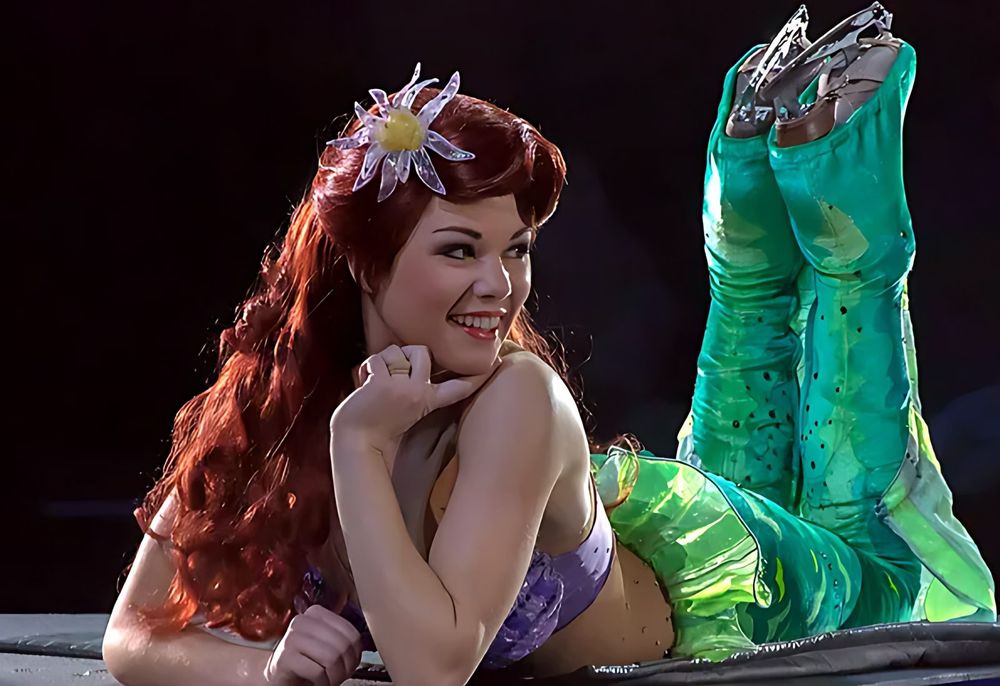 Ariel with red hair and a green sequin tail lying on the ice, Disney On Ice: Worlds of Fantasy. Costume design by Cynthia Nordstrom