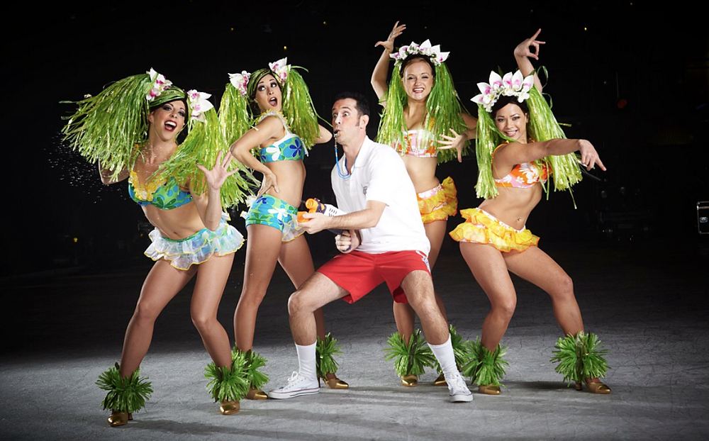 Hula skaters in grass skirts and flower crowns around a tourist in red shorts, Holiday On Ice: Speed. Costume design by Cynthia Nordstrom
