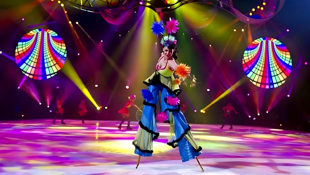 Stilt walker in a flowing blue and yellow costume with a flower headdress, Holiday On Ice: Speed. Costume design by Cynthia Nordstrom