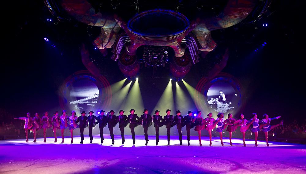 Kick line of skaters in pink and purple under a lit arena rig, Holiday On Ice: Speed. Costume design by Cynthia Nordstrom