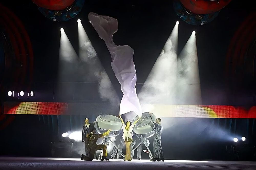 Performer suspended in white fabric above dancers in white, smoky spotlights, Holiday On Ice: Speed. Costume design by Cynthia Nordstrom