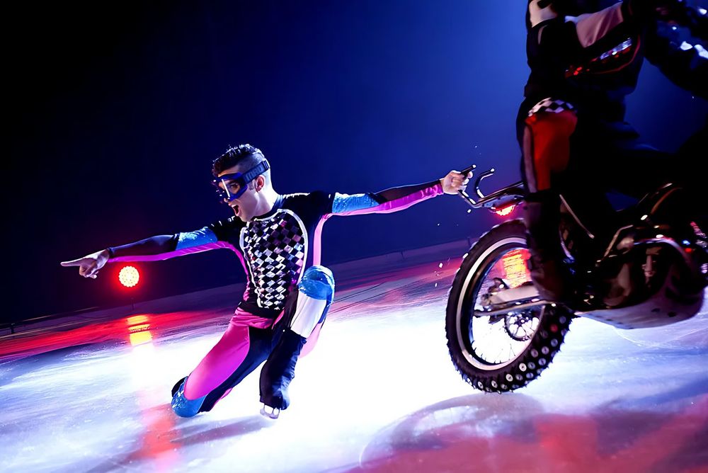 Skater in a houndstooth and neon racing suit beside a stunt motorcycle, Holiday On Ice: Speed. Costume design by Cynthia Nordstrom