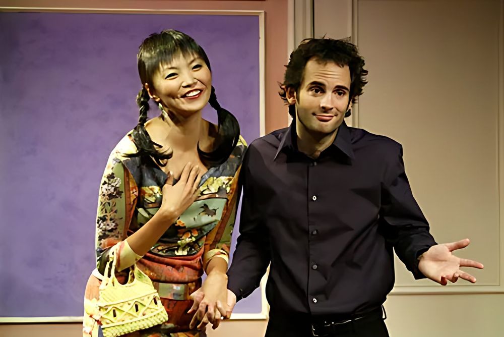 Woman in a patterned dress with pigtails and a man in a black shirt, Jewtopia. Costume design by Cynthia Nordstrom