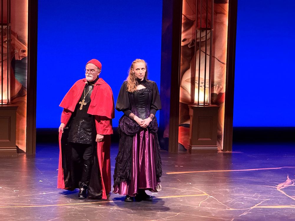 Cardinal in red robes beside a woman in a black and purple gown, The Three Musketeers. Costume design by Cynthia Nordstrom