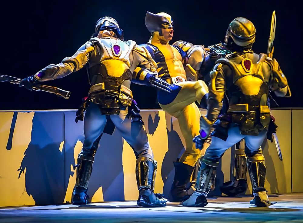 Wolverine in yellow and blue fighting armored henchmen in gold, Marvel Universe Live. Costume design by Cynthia Nordstrom