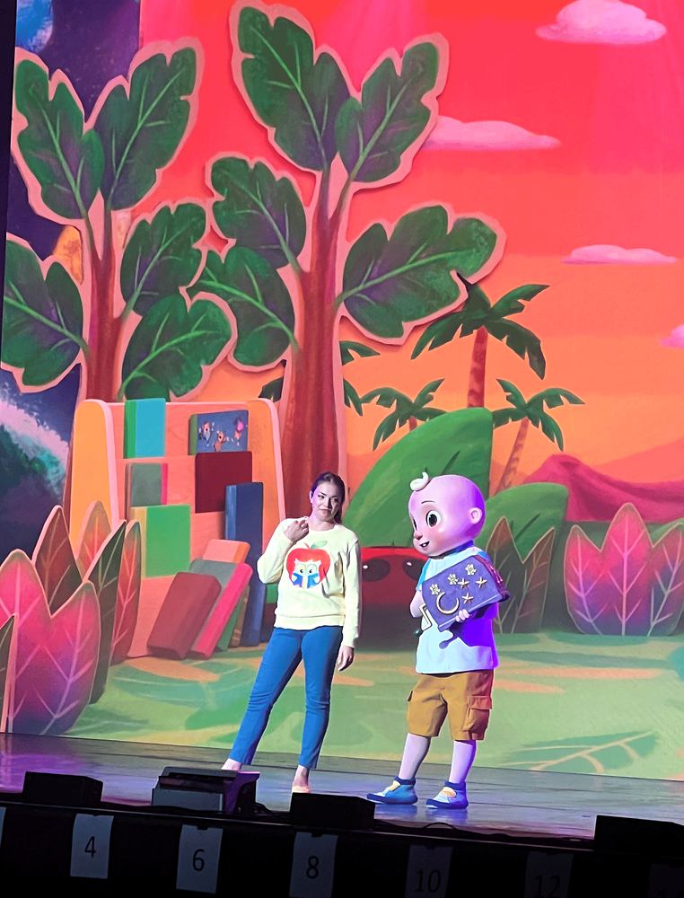 Host in jeans and a white tee with a character in a jungle set, CoComelon Live!. Costume design by Cynthia Nordstrom