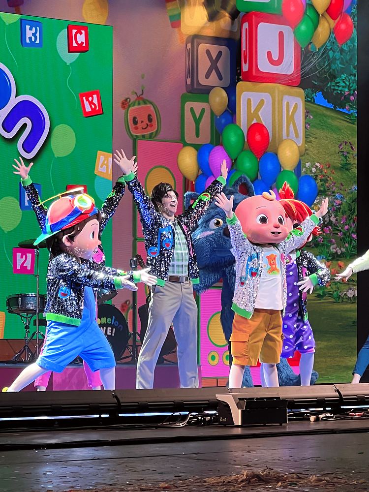 JJ and cast in colorful patterned jackets and hats on an alphabet block set, CoComelon Live!. Costume design by Cynthia Nordstrom