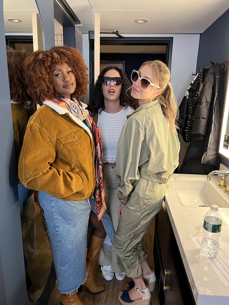 Three women in styled looks for the Motto by Hilton commercial: a mustard corduroy jacket with a denim skirt, a white top with sunglasses, and an olive utility jumpsuit. Wardrobe design by Cynthia Nordstrom