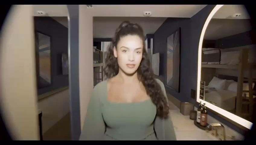 A woman with long dark curls in a sage green top walks through a hotel room. Wardrobe design by Cynthia Nordstrom