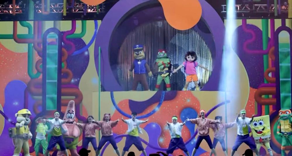 Nickelodeon Live: Está en Ti: the company in pink, white and purple dancewear with SpongeBob, Patrick, Rubble and Raphael as Chase, a Ninja Turtle and Dora appear in a round window above. Costume design by Cynthia Nordstrom