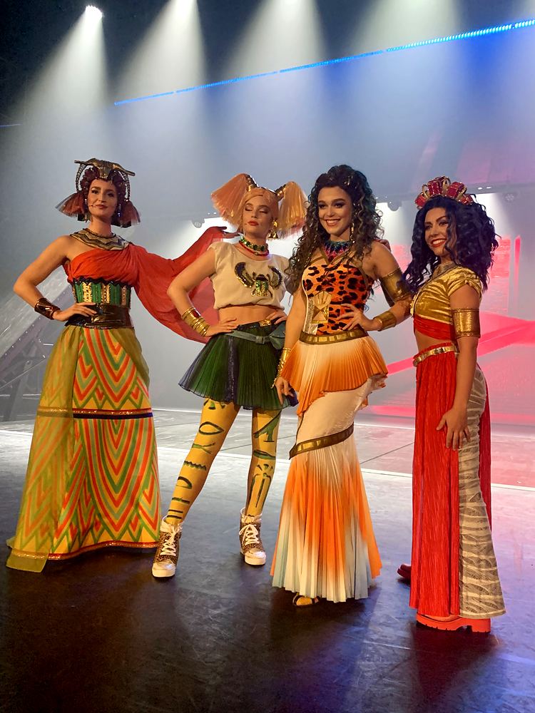 Four women in patterned gowns, green skirt and red gown in a lineup, ONE de Musical. Costume design by Cynthia Nordstrom