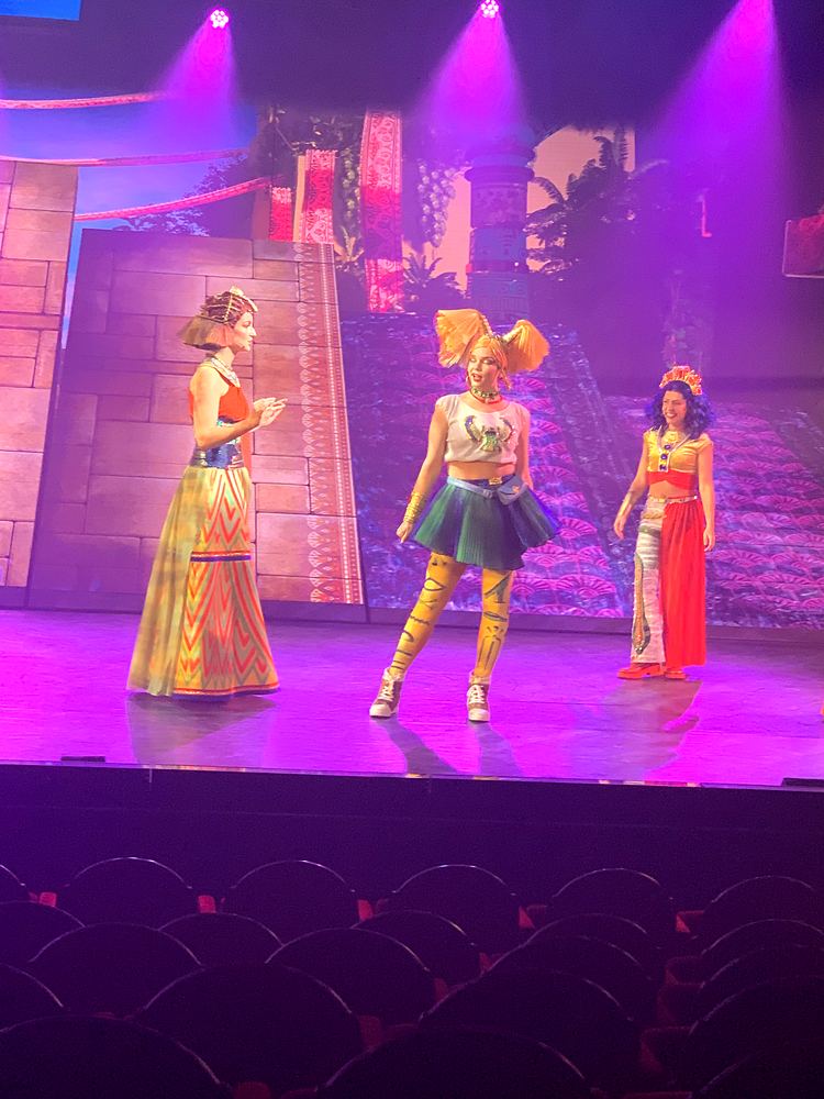 Three women in gowns and a short green skirt on the temple steps set, ONE de Musical. Costume design by Cynthia Nordstrom