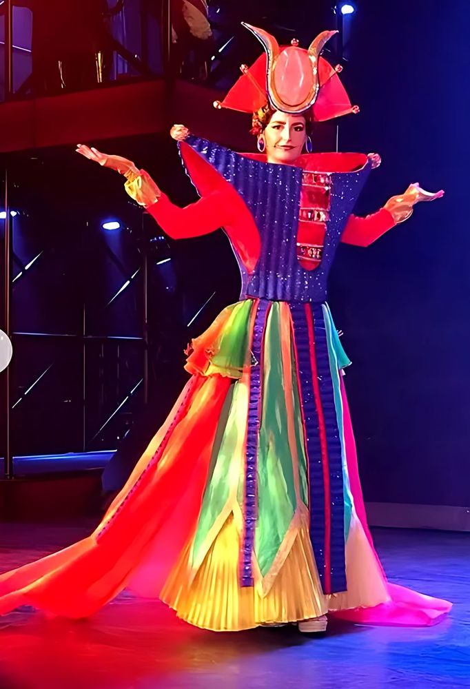 ONE de Musical: a performer in a red and blue gown with a crown headdress. Costume design by Cynthia Nordstrom