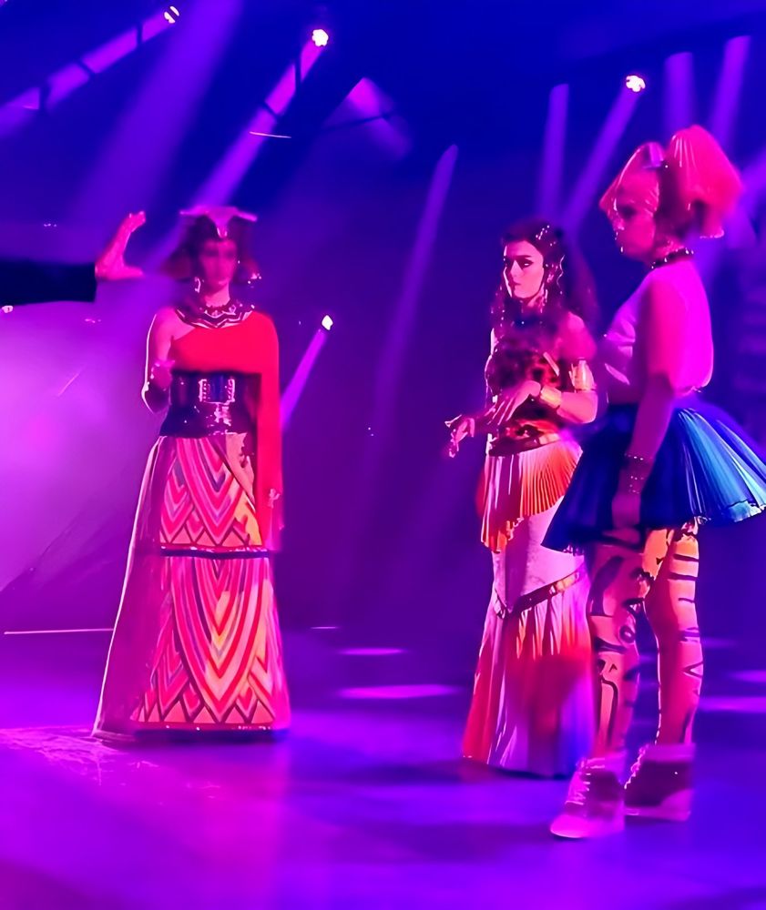 ONE de Musical: three performers on stage under purple light. Costume design by Cynthia Nordstrom