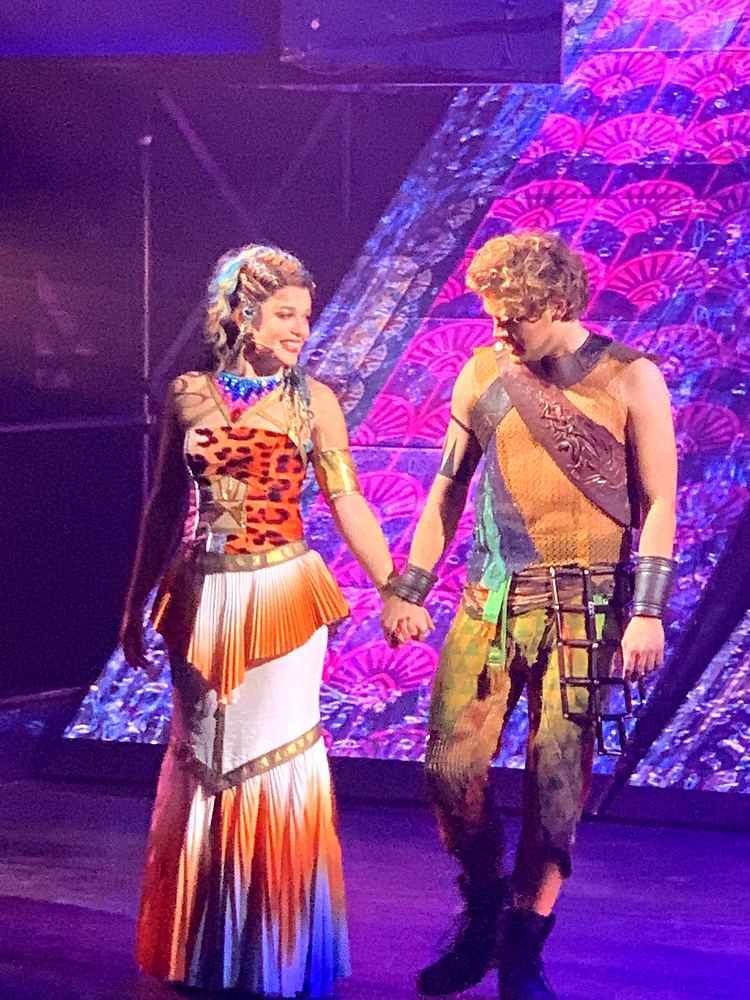 Woman in a leopard and white pleated gown holding hands with a man in leather, ONE de Musical. Costume design by Cynthia Nordstrom