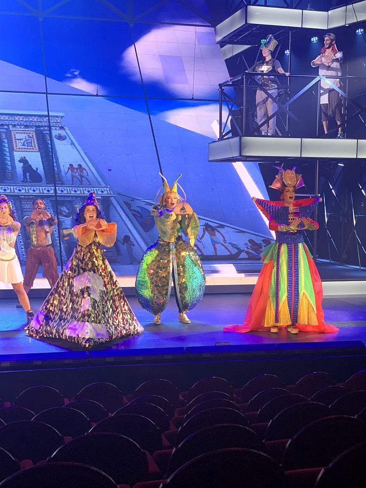 Three women in patterned gowns center stage with the ensemble above, ONE de Musical. Costume design by Cynthia Nordstrom