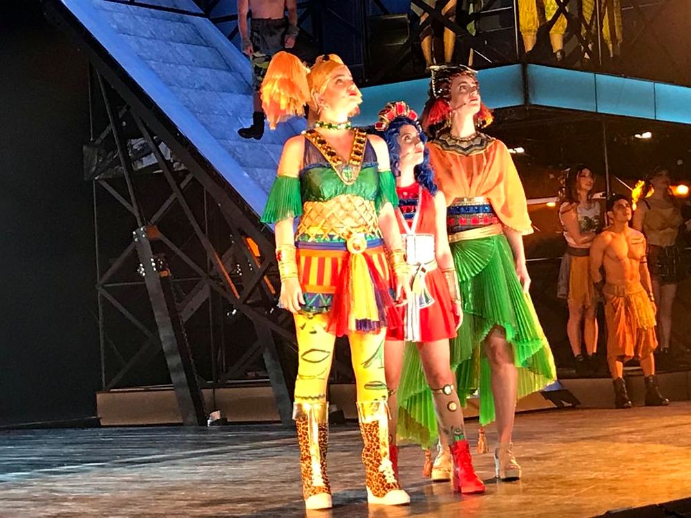 Three women in bright patchwork costumes and leopard boots on stage, ONE de Musical. Costume design by Cynthia Nordstrom