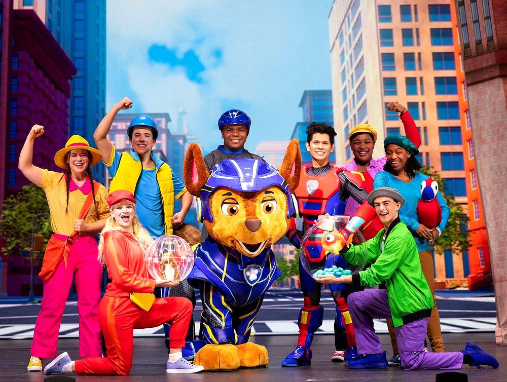 PAW Patrol Live! A Mighty Adventure: Chase in blue Mighty Pups armor with Ryder and Adventure City townspeople in bright pink, yellow and green. Costume design by Cynthia Nordstrom