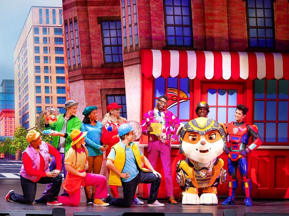 PAW Patrol Live! A Mighty Adventure: Rubble in gold armor with Ryder and townspeople, one in a candy-covered pink suit holding a pizza box. Costume design by Cynthia Nordstrom