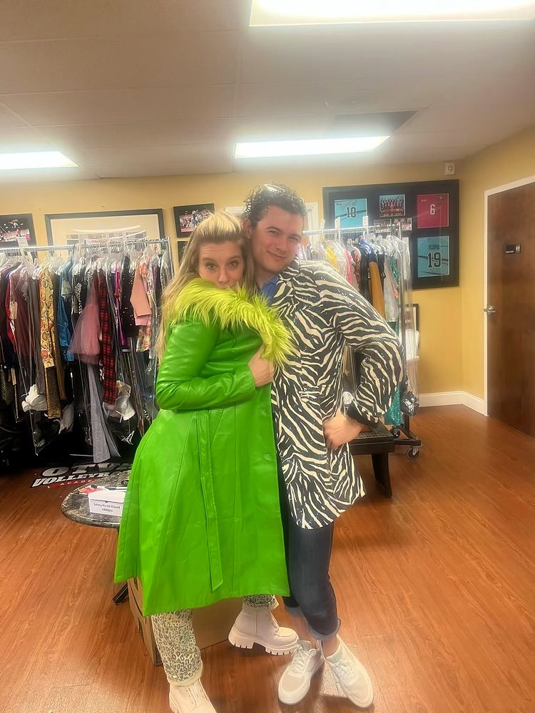 Cynthia Nordstrom in a green coat with a fur collar, posing with a friend in a costume shop