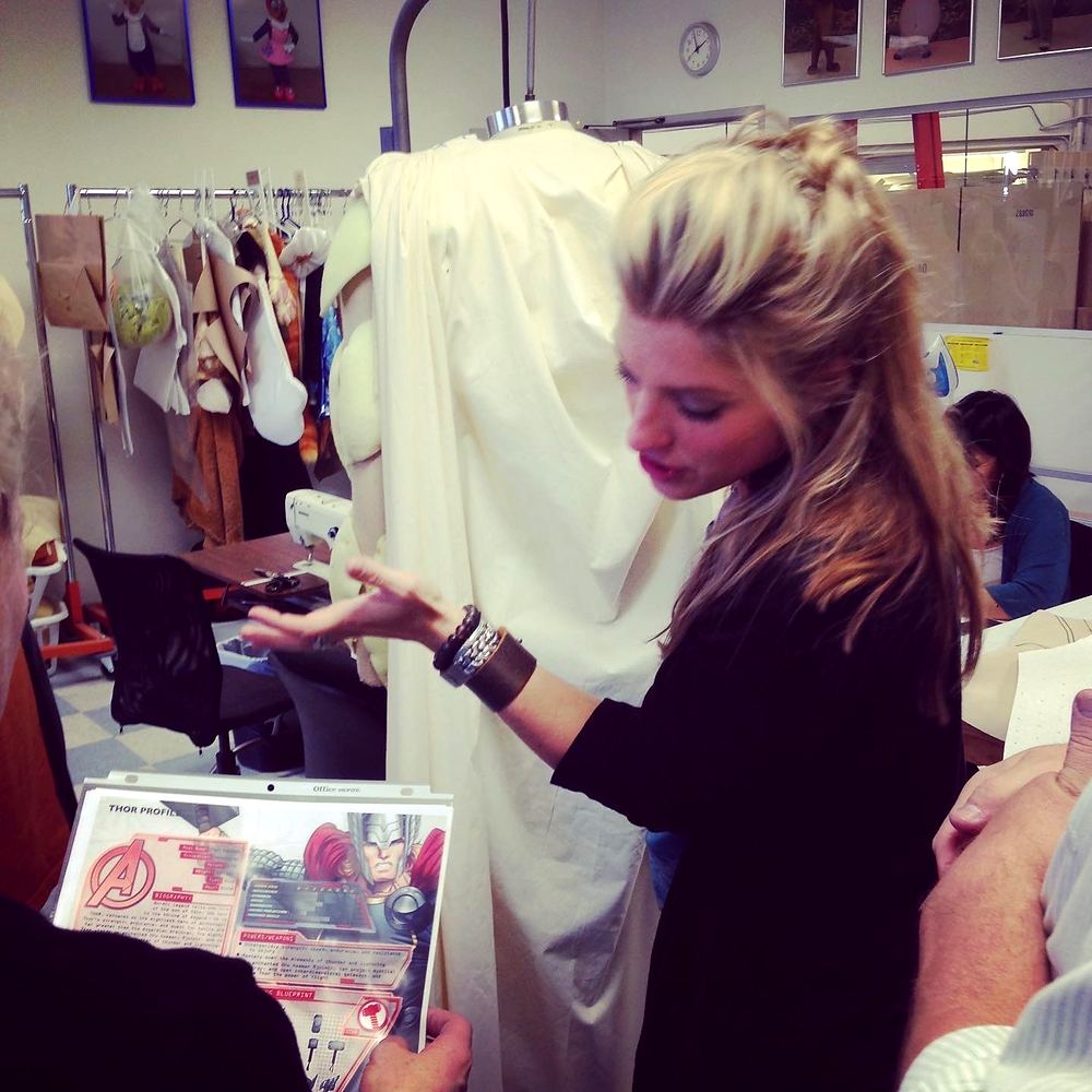 Cynthia Nordstrom holding a costume sketch beside a garment on a dress form