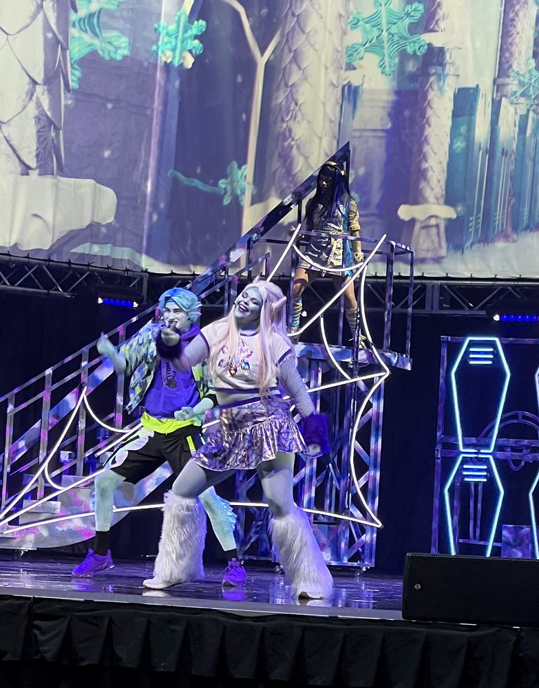 Two students in a lime top and a sparkly silver dress on a web set, Monster High Live. Costume design by Cynthia Nordstrom