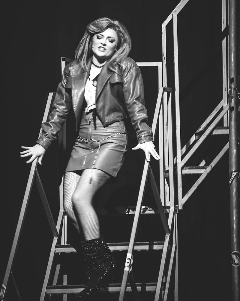 Woman in a leather jacket and mini skirt on a stage stair unit, Rock of Ages. Costume design by Cynthia Nordstrom