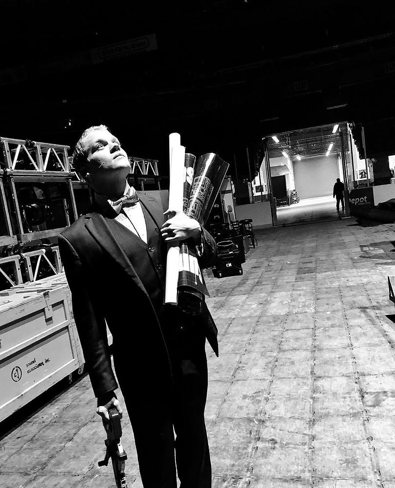 Performer in a black tuxedo holding a rolled poster backstage, Rock of Ages. Costume design by Cynthia Nordstrom