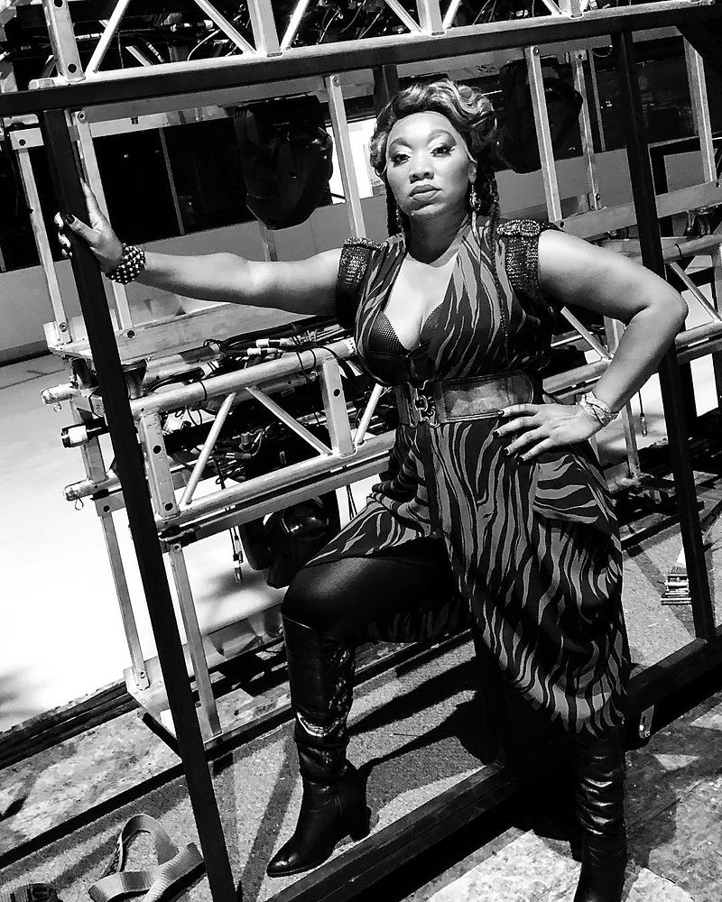 Woman in a striped wrap dress and tall boots posing on stage truss, Rock of Ages. Costume design by Cynthia Nordstrom