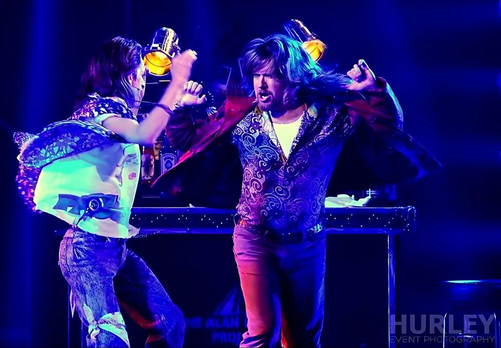 Two rockers in sequined and printed jackets with glasses under blue light, Rock of Ages. Costume design by Cynthia Nordstrom