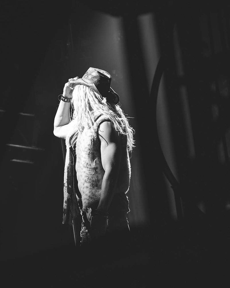 Rocker in a hat and long fringed vest under a spotlight, black and white, Rock of Ages. Costume design by Cynthia Nordstrom