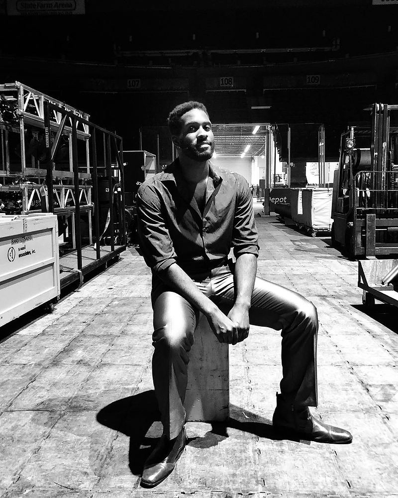 Man in a dark shirt and slacks sitting on a crate backstage, Rock of Ages. Costume design by Cynthia Nordstrom