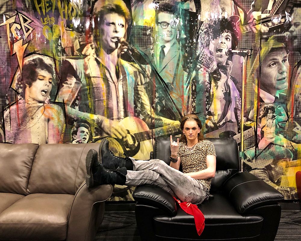 Rocker in leopard print with feet up on a couch before a rock mural, Rock of Ages. Costume design by Cynthia Nordstrom