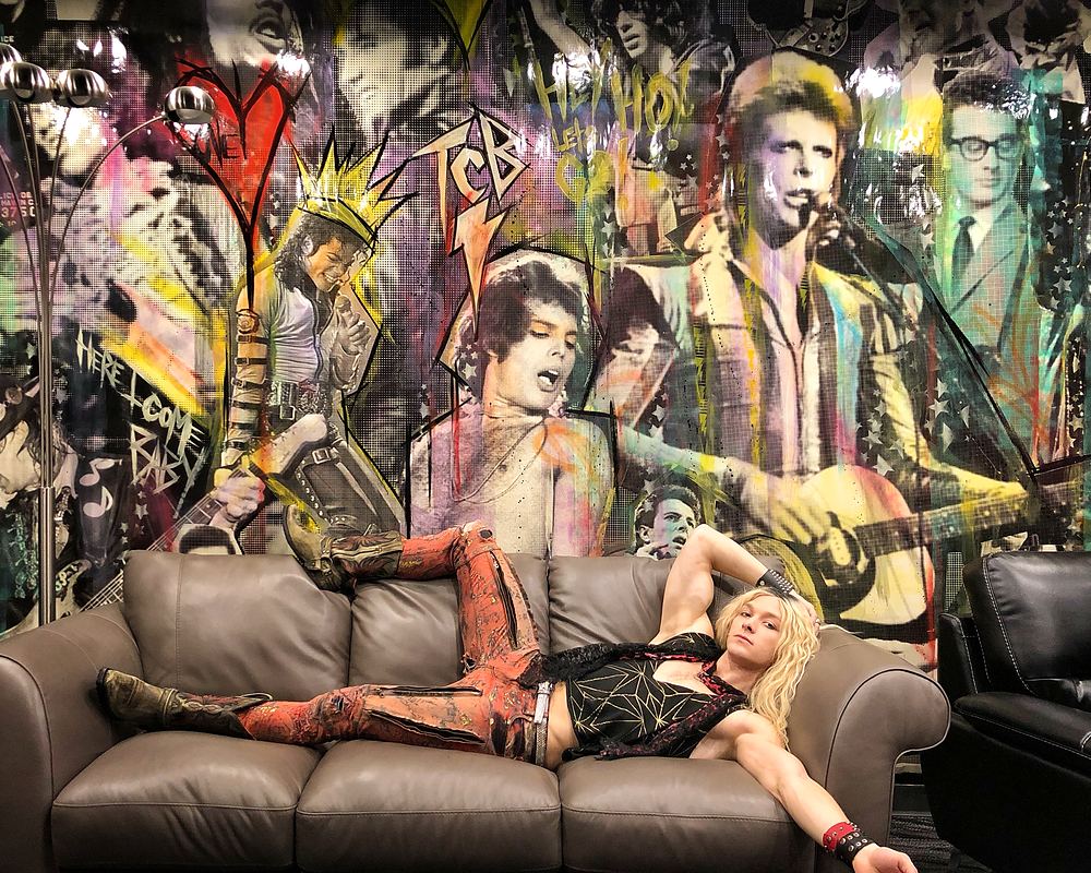 Rocker in leather and leopard print sprawled on a couch before a rock mural, Rock of Ages. Costume design by Cynthia Nordstrom