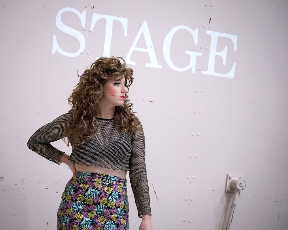 Woman in a sheer crop top and neon print skirt with big curls, Rock of Ages. Costume design by Cynthia Nordstrom