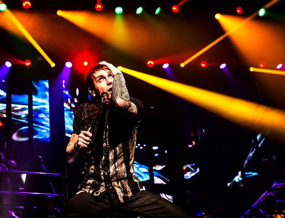 Tattooed singer in a black patterned shirt under orange lights, Rocktopia. Costume design by Cynthia Nordstrom