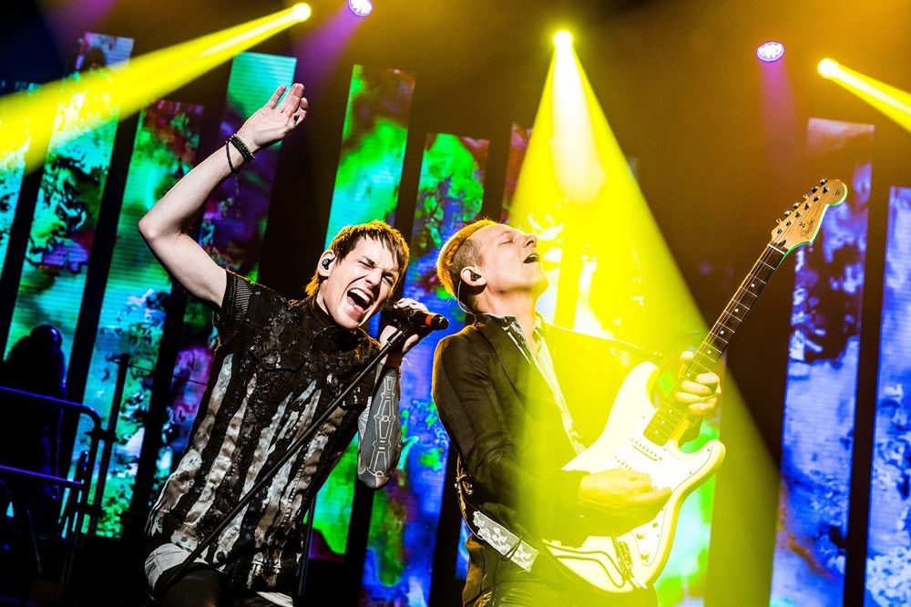 Singer and guitarist in black embellished shirts under yellow lights, Rocktopia. Costume design by Cynthia Nordstrom