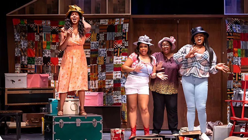 Four women in a peach sundress, pink shorts, a leopard blouse and a plaid shirt with hats on a patchwork quilt set, Sistas The Musical. Costume design by Cynthia Nordstrom