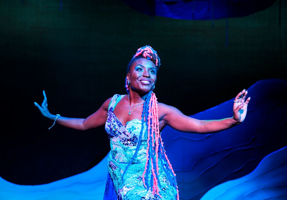 Woman with long pink braids in a blue sequin gown under blue light, Spells of the Sea. Costume design by Cynthia Nordstrom