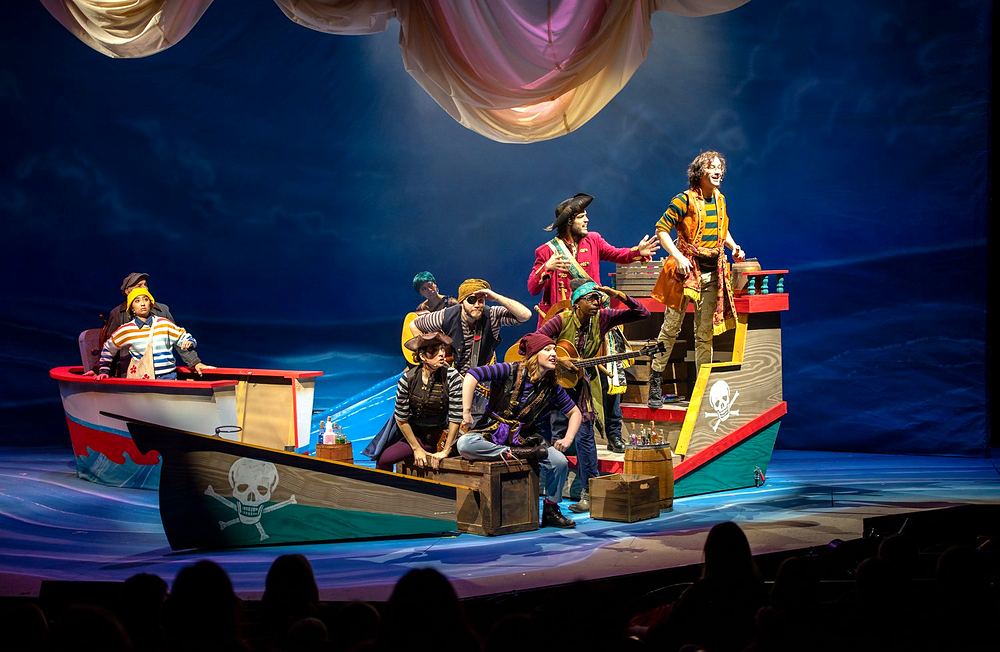 Pirate crew in striped shirts and bandanas aboard a small boat set, Spells of the Sea. Costume design by Cynthia Nordstrom