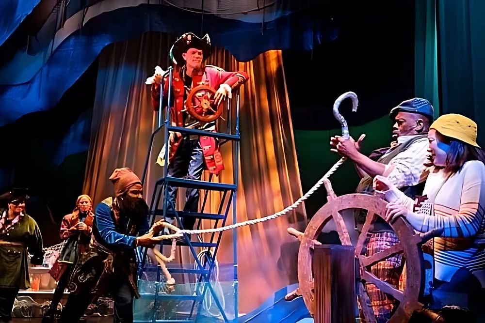 Pirate captain on a ladder with crew in striped shirts at the ship wheel, Spells of the Sea. Costume design by Cynthia Nordstrom