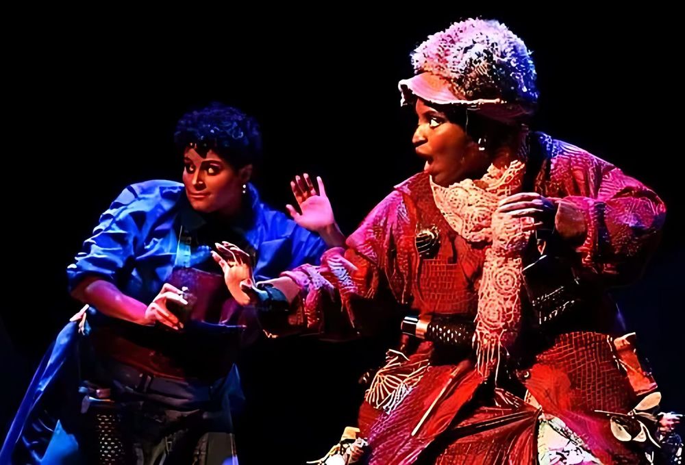 Shopkeeper in a red knit coat and hat with a girl in a blue jacket, Spells of the Sea. Costume design by Cynthia Nordstrom