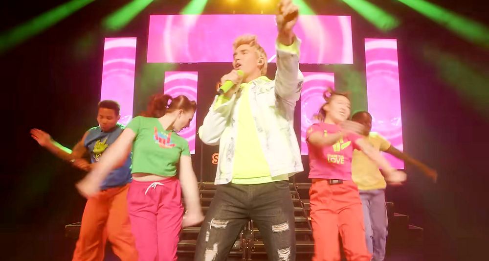 Stephen Sharer in a white tee with dancers in bright colored outfits on a pink lit stage, Stephen Sharer: Share the Love Tour. Co-costume design by Cynthia Nordstrom