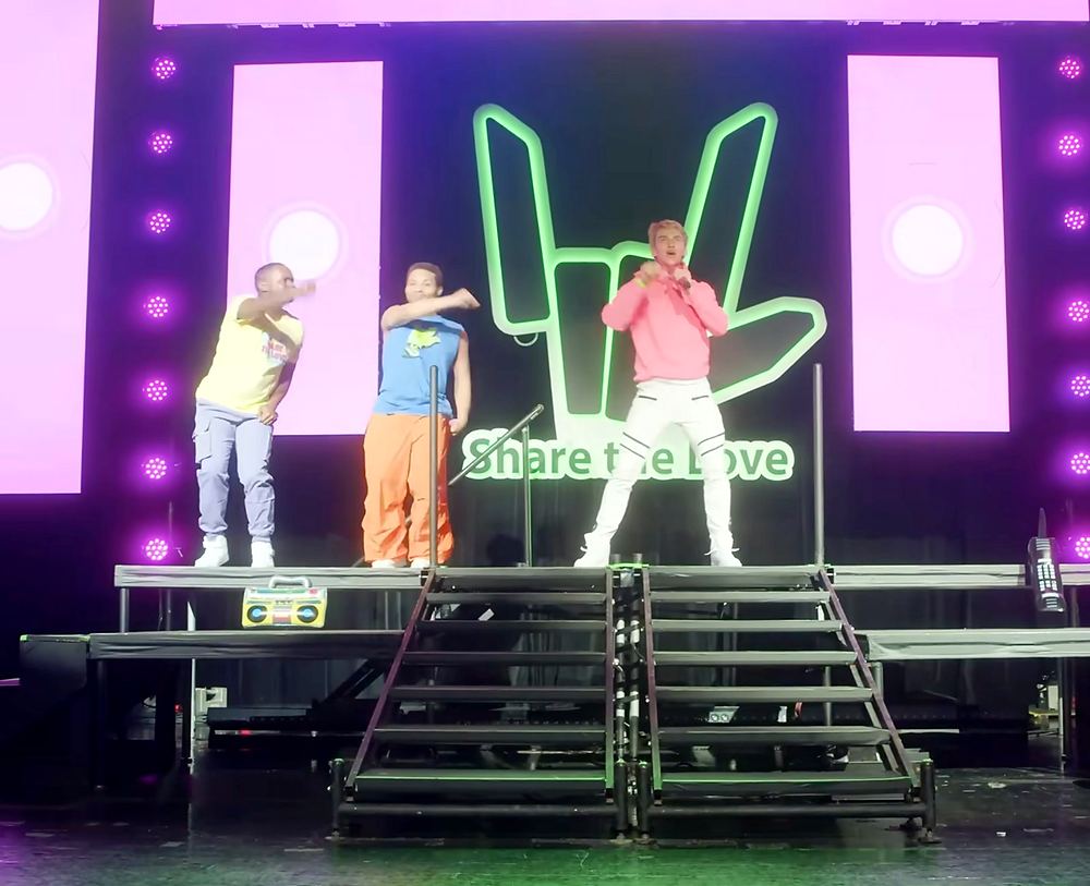 Dancers in neon tees and white pants on a pink and green lit stage with the Share the Love hand logo, Stephen Sharer: Share the Love Tour. Co-costume design by Cynthia Nordstrom