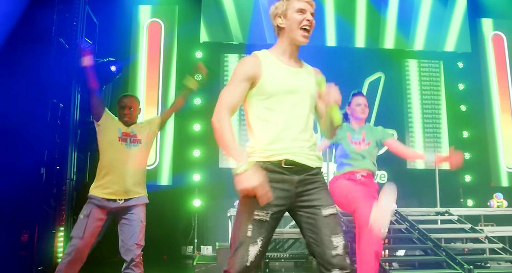 Stephen Sharer in a green tee and silver pants with dancers in neon colors on a pink and green stage, Stephen Sharer: Share the Love Tour. Co-costume design by Cynthia Nordstrom