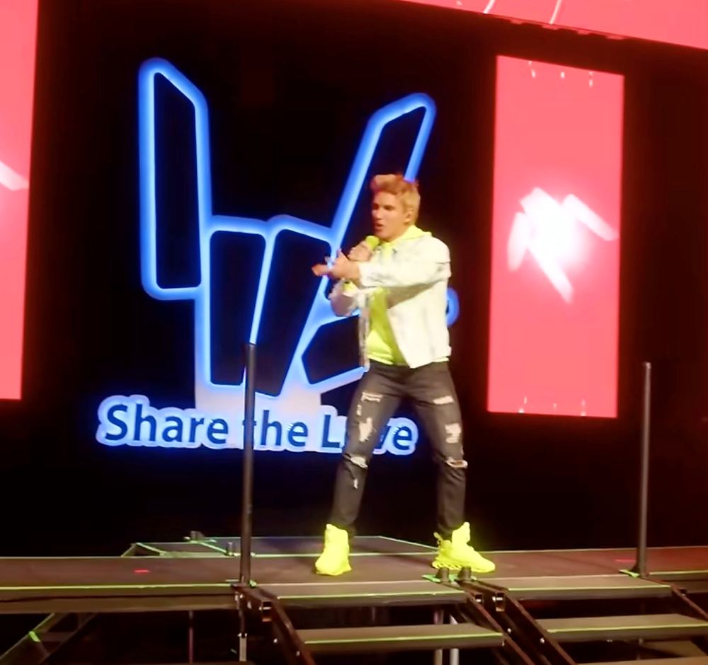 Stephen Sharer in a white tee and gray pants with neon green sneakers beside the Share the Love hand logo, Stephen Sharer: Share the Love Tour. Co-costume design by Cynthia Nordstrom