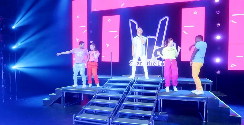 Dancers in neon colors spread across a pink lit stage with a hand logo screen, Stephen Sharer: Share the Love Tour. Co-costume design by Cynthia Nordstrom