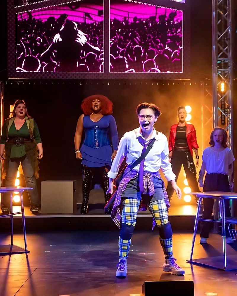 Teen in a white shirt and plaid pants leading the cast in a song, SuperYou. Costume design by Cynthia Nordstrom
